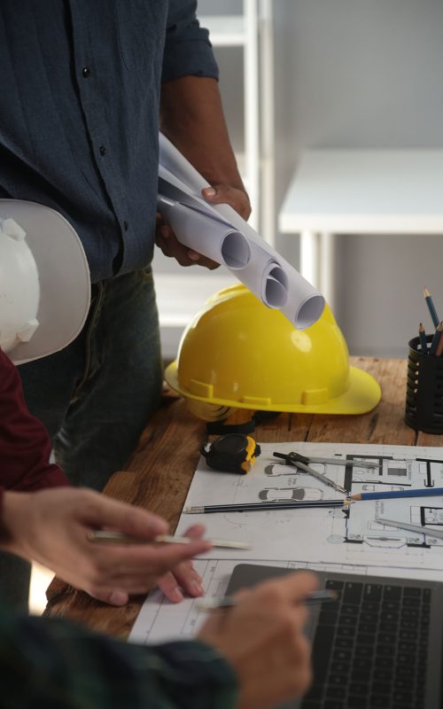 Engineers are consulting the team to design an architectural structure for clients with blueprints and building models to work at office.